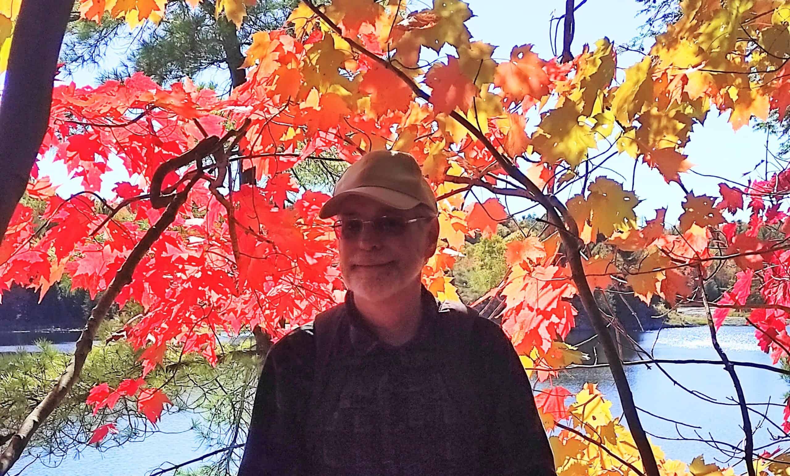 Autumn portrait of Mark Hathaway under colourful fall leaves by a river.